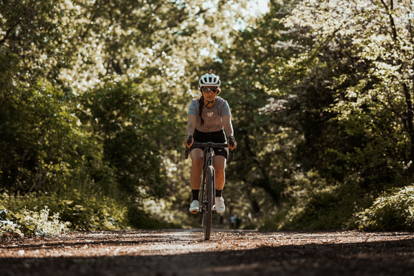 Femme à vélo dans la fôret. Elle est équipée d'un casque, d'un t-shirt en mesh violet et d'un cuissard de cyclisme court.