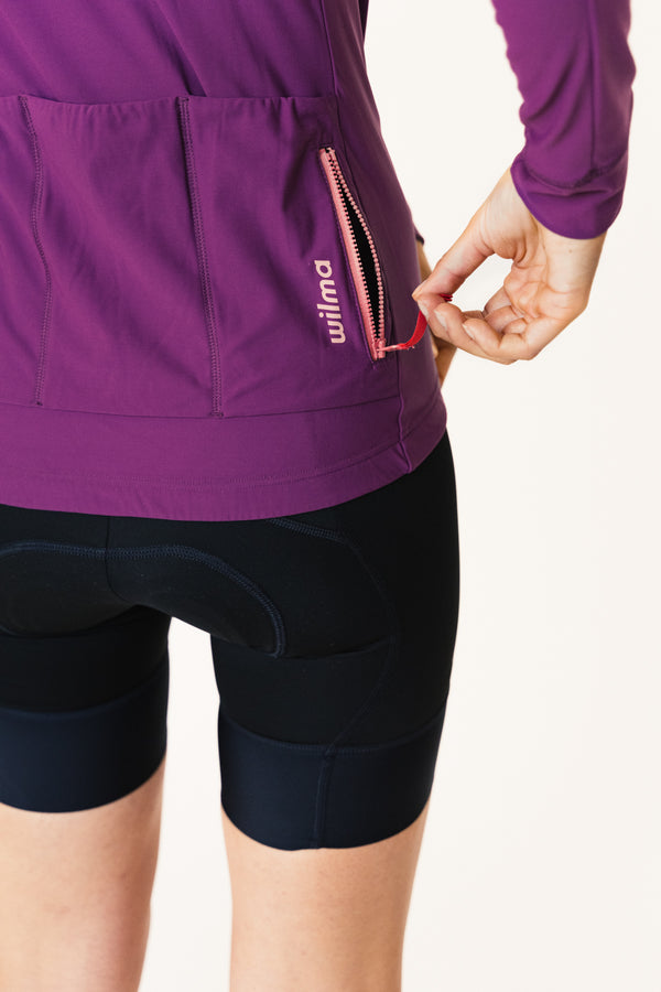Femme portant le Jersey d'hiver violet d ela marque de vêtements de cyclisme Wilma. Vue des poches arrières et de la poche zipée.