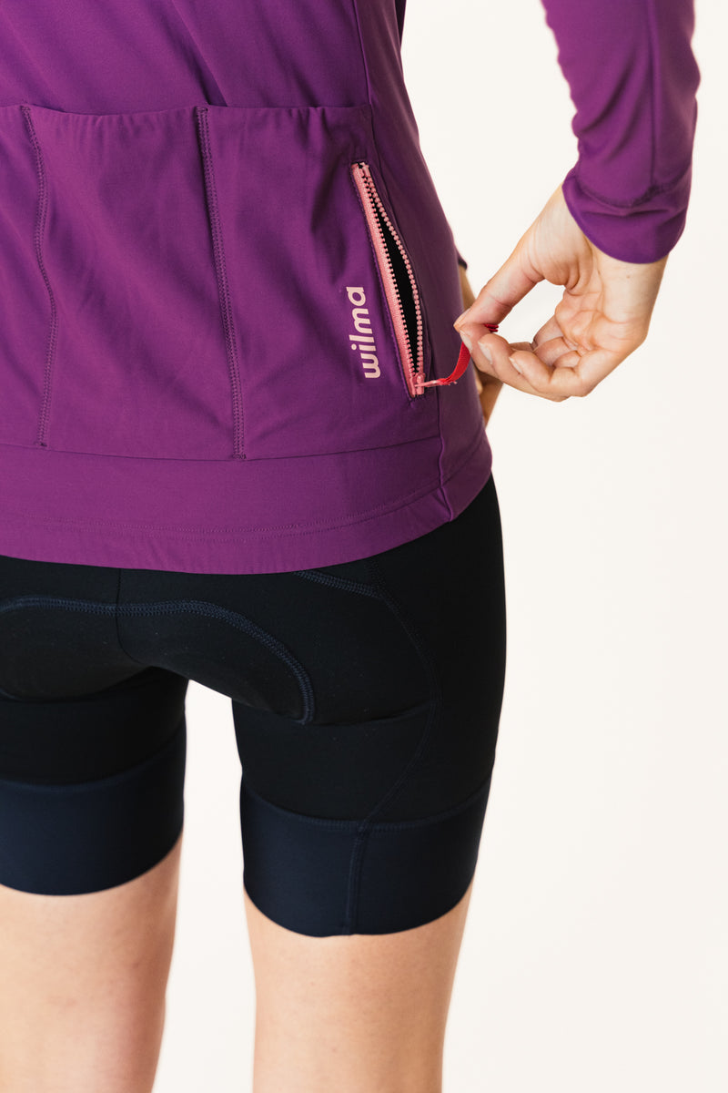 Femme portant le Jersey d'hiver violet d ela marque de vêtements de cyclisme Wilma. Vue des poches arrières et de la poche zipée. 