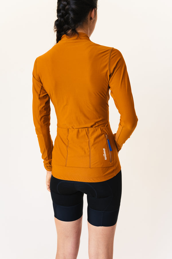 Femme portant un jersey de cyclisme couleur camel, vu de dos avec trois poches à l'arrière dont une zippée #color_Camel